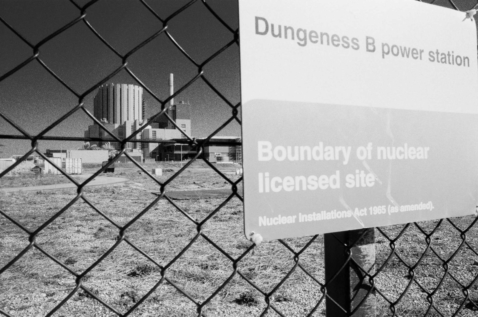 Dungeness B nuclear power station viewed through chain-link fence, boundary of nuclear licensed site sign, Kent, black and white film photography