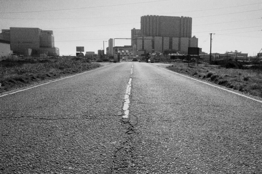 Empty road leading directly to Dungeness nuclear power station entrance, low angle perspective, road markings, Kent, black and white film photography