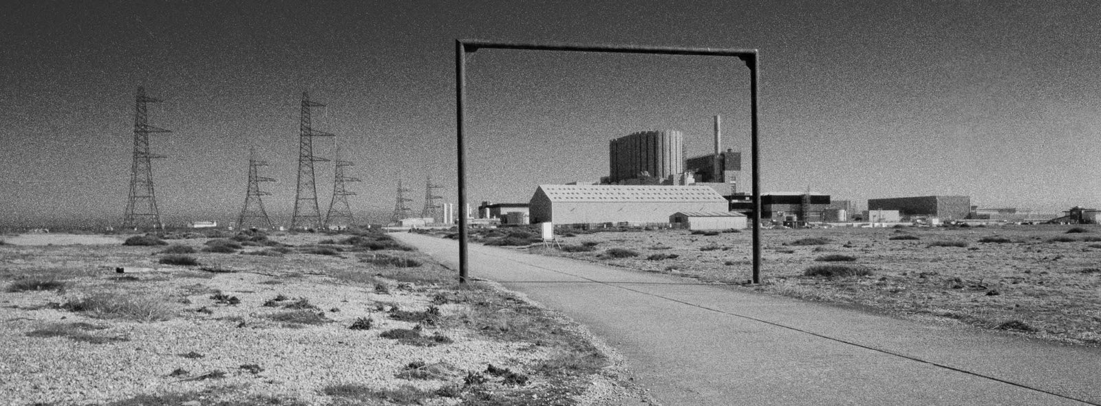 Abandoned metal frame structure on Dungeness shingle headland with nuclear power station and electricity pylons, panoramic black and white film photography, Kent