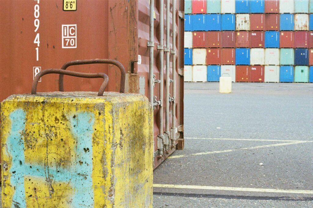 A weathered yellow bollard in the foreground with rows of coloured shipping containers stacked behind at the Port of Felixstowe