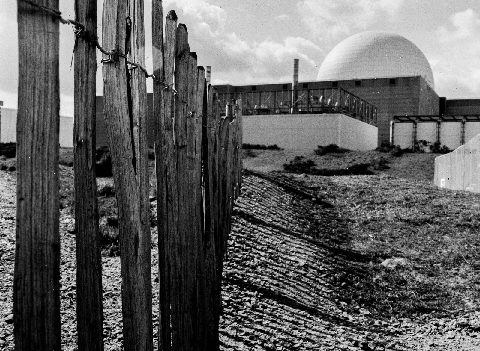 Weathered wooden fence posts on the shingle beach at Sizewell, with the luminescent dome of Sizewell B nuclear reactor behind