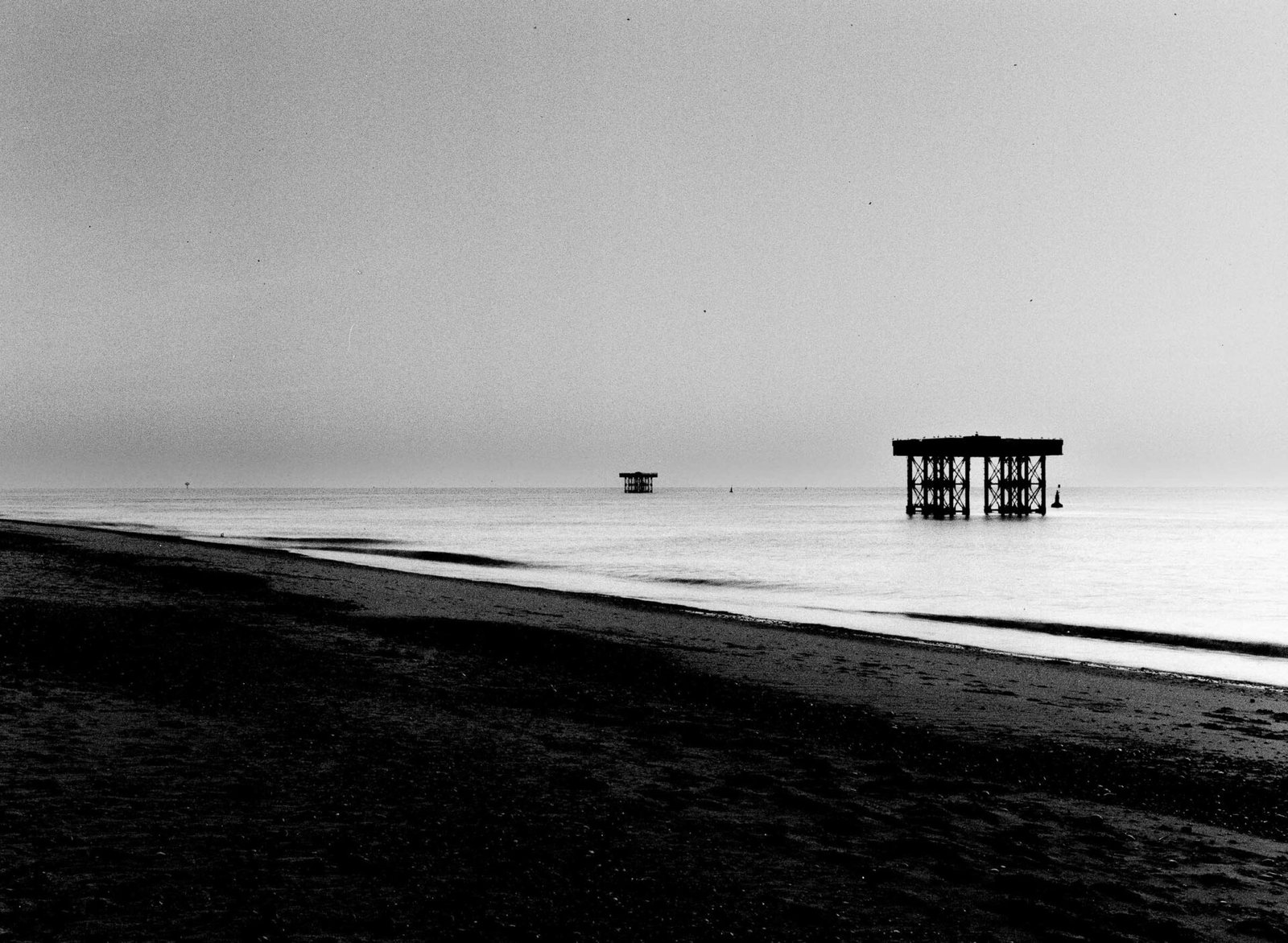 Two derelict industrial structures standing in a calm sea off Sizewell Beach, Suffolk, silhouetted against a pale sky