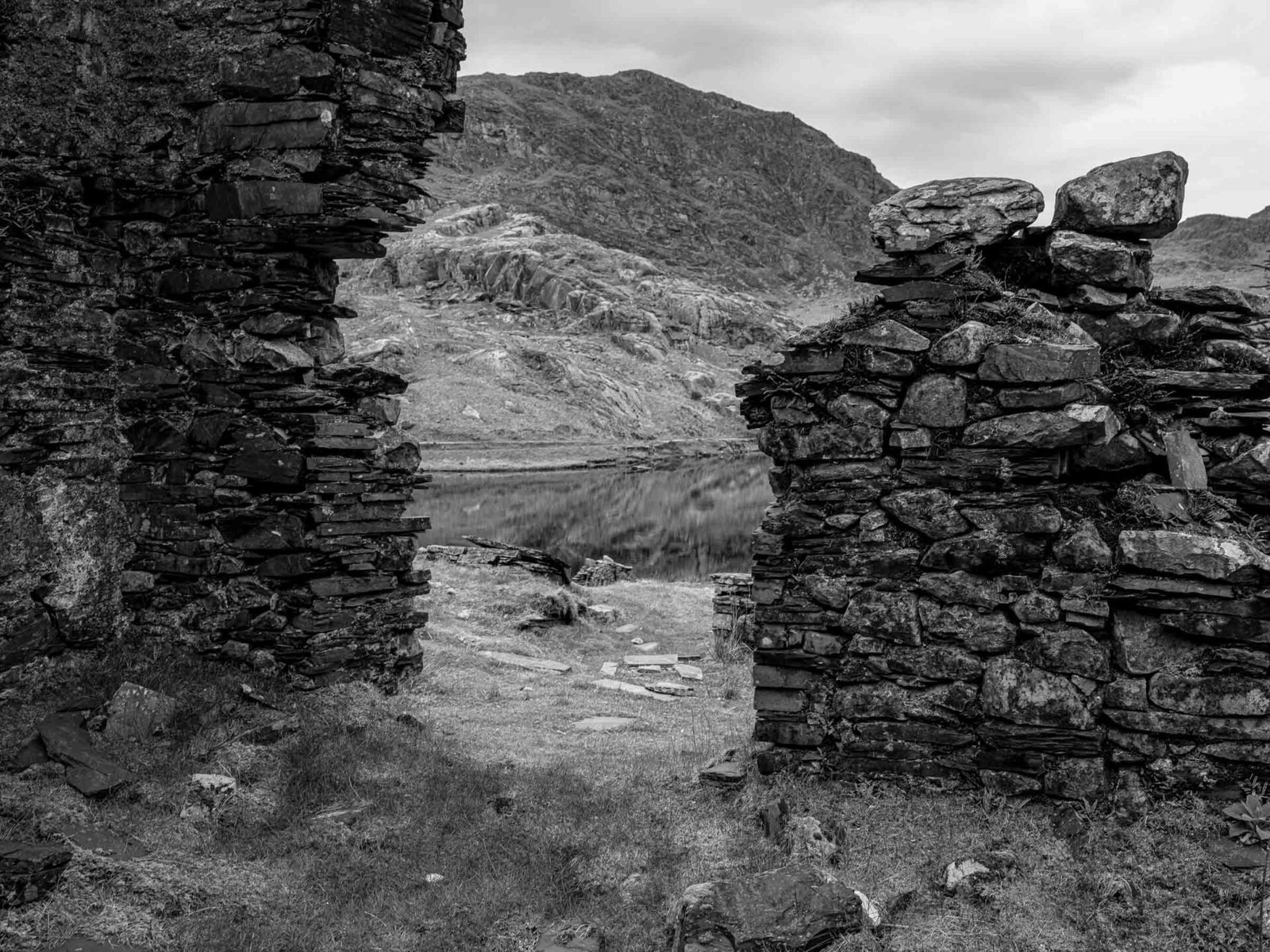 View through a ruined doorway at Cwmorthin Quarry, framing a still lake and mountain beyond.