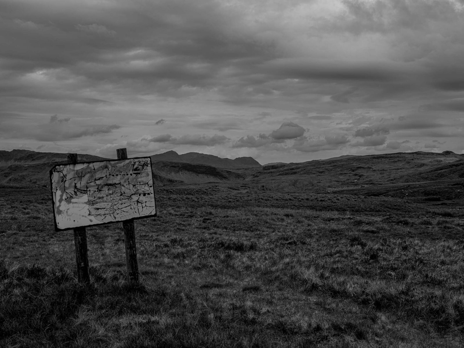 A blank, weathered sign with peeling paint standing in open moorland at Conglog Quarry, its message long gone.