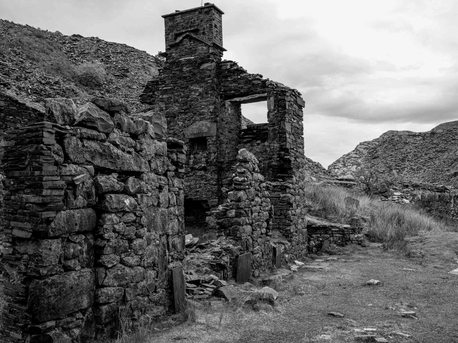 A ruined building at Cwmorthin Quarry with a surviving chimney and an empty window, set against a hillside of slate waste.