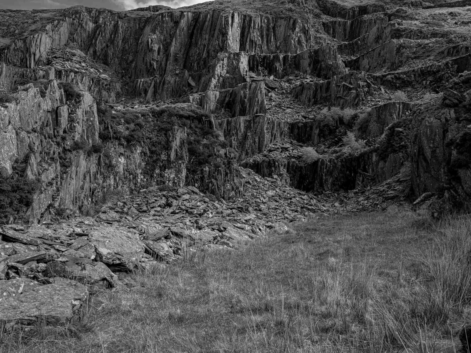 A vertical quarry face of cut slate at Gorseddau, its terraced ledges and rubble showing where the rock was worked away.