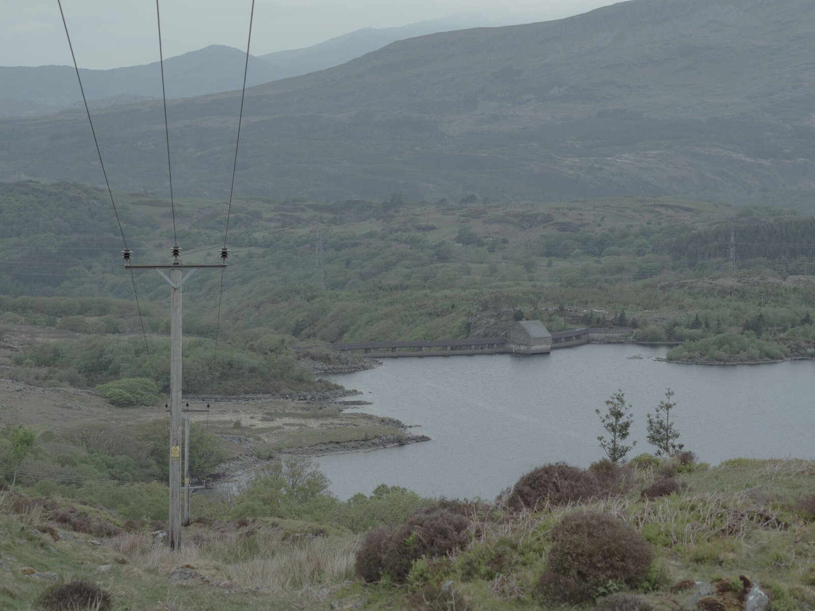 Electricity pylon in foreground with the Maentwrog dam and reservoir visible in the valley below, Eryri