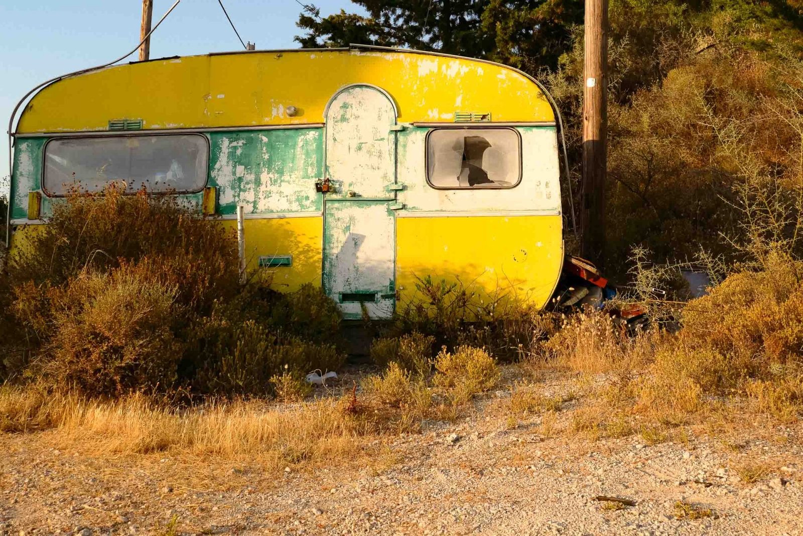 Abandoned yellow and green vintage caravan with broken window in dry scrubland, Lefkada, Greece