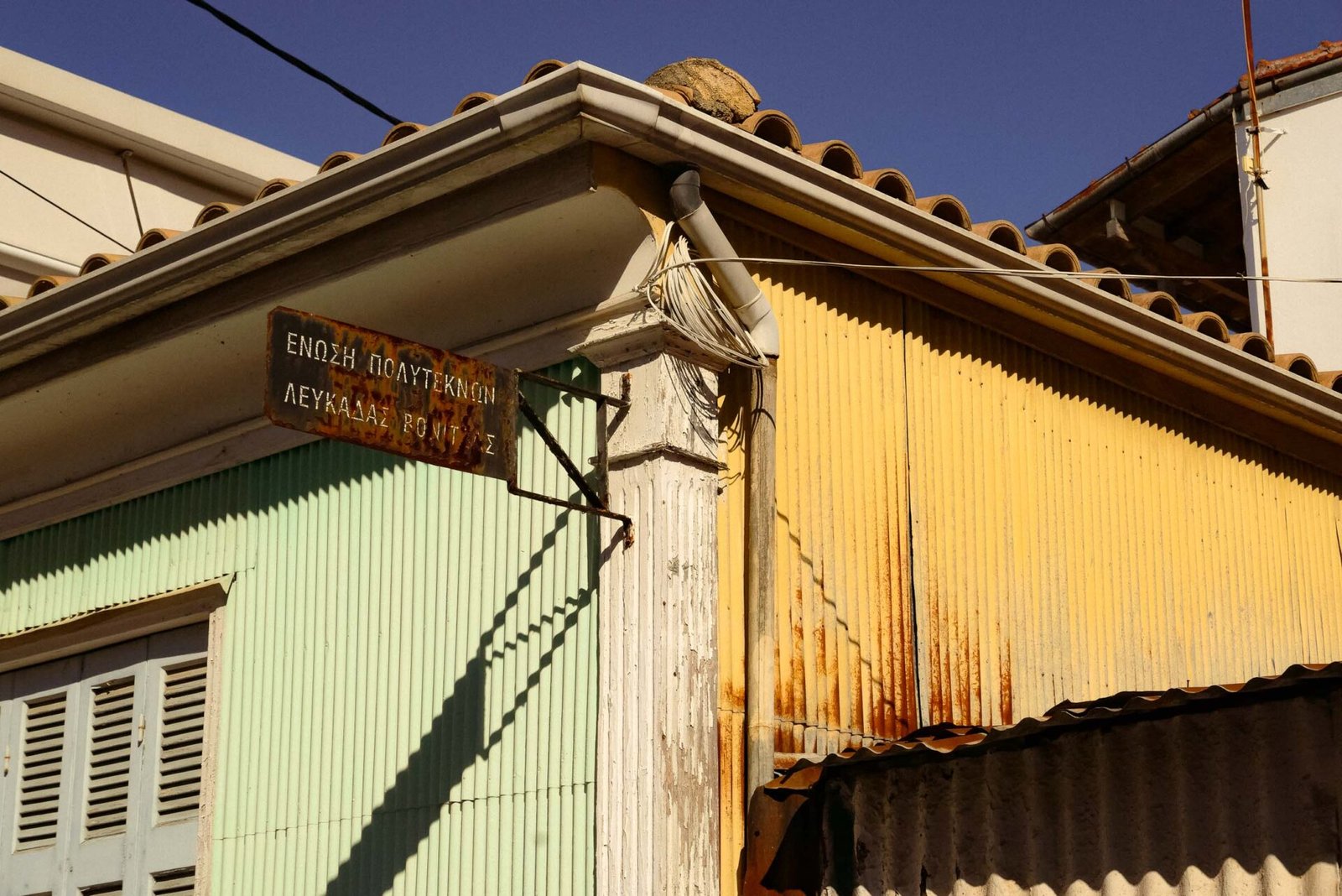 Weathered green and yellow corrugated iron building corner with old Greek signage, Lefkada Town, Greec