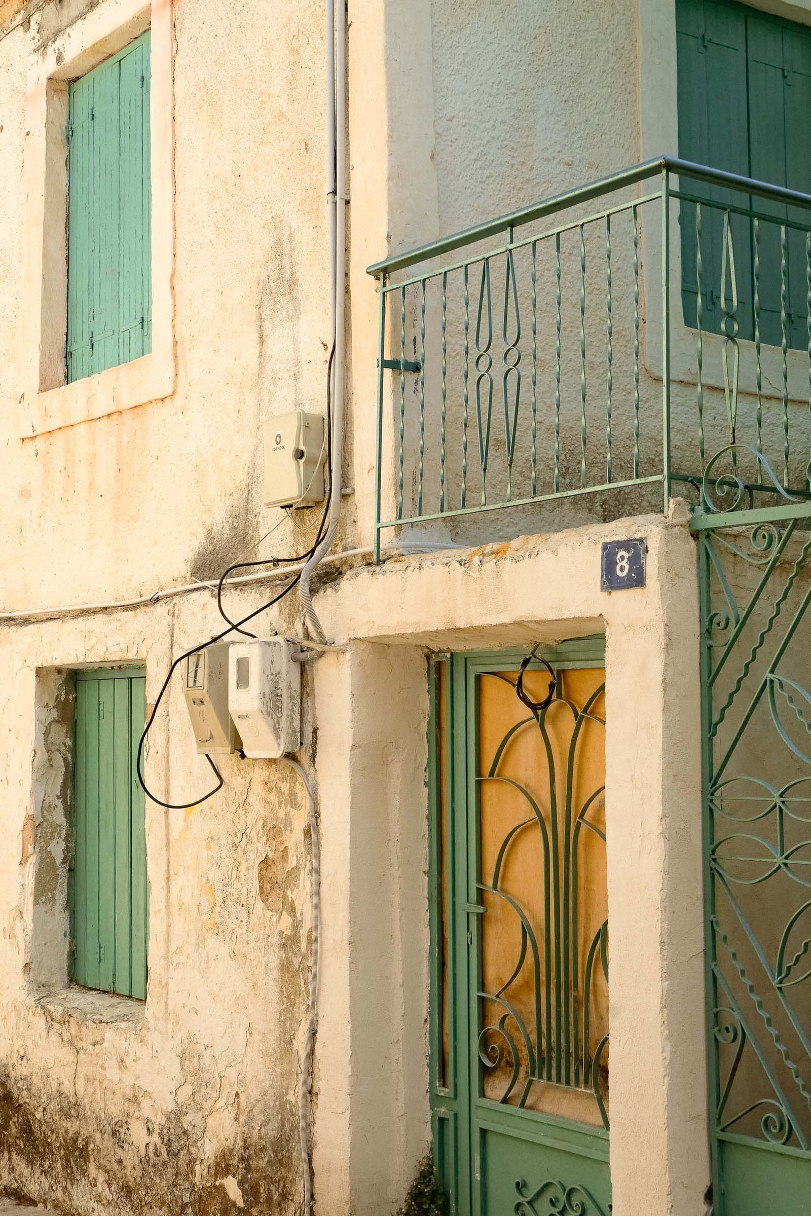 Weathered pastel yellow house with green shutters and ironwork balcony, Lefkada Town, Greece